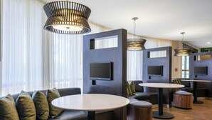 Un moderno hall de hotel con un sofá, mesas redondas y un televisor montado en la pared.