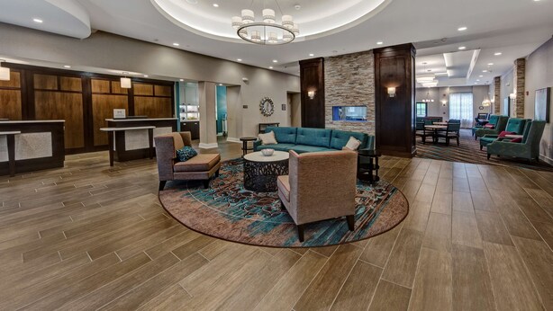 A spacious lobby with a reception desk, seating area with sofas and chairs, a large chandelier, and a stone accent wall.