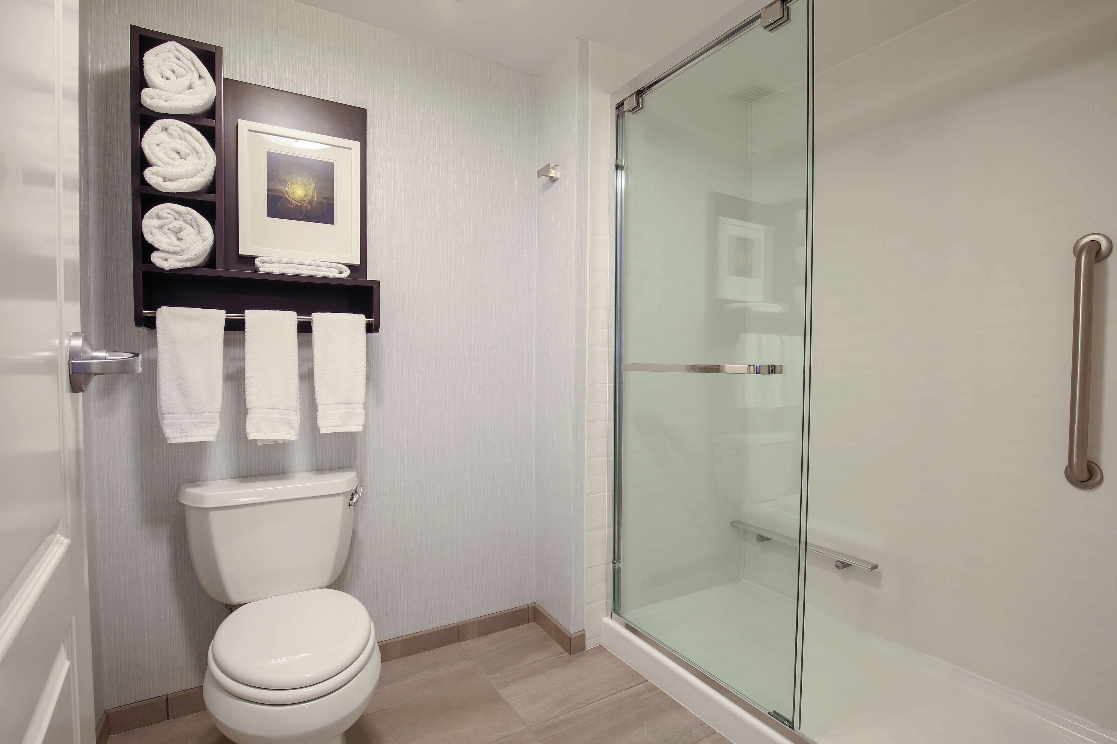 Un baño moderno con inodoro, cabina de ducha de vidrio y un perchero con toallas dobladas.