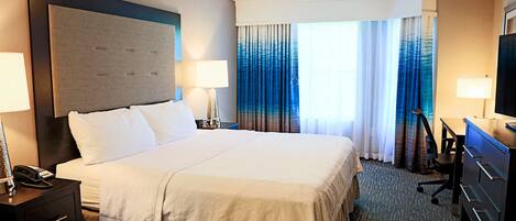Quarto de hotel com uma cama grande, duas mesas de cabeceira com abajures, uma escrivaninha com cadeira e um ventilador de teto.