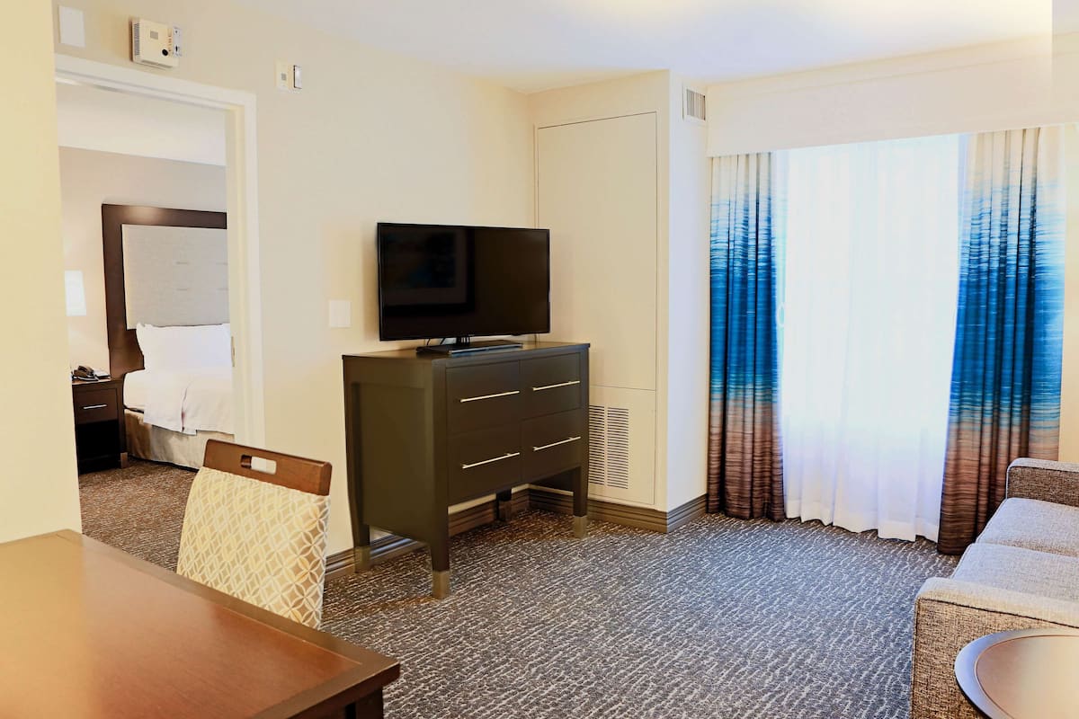 Ein Hotelzimmer mit einem Bett, einem Fernseher auf einer Kommode, einem Esstisch und einem Sofa.