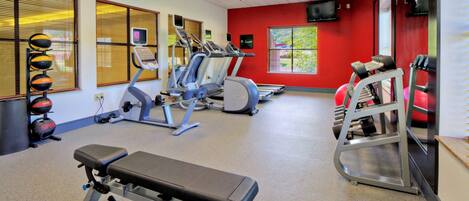 Un gimnasio con equipo de ejercicio, una banca y una pared roja.
