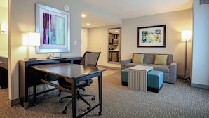 A hotel room with a desk, a sofa, a small ottoman, and two lamps.