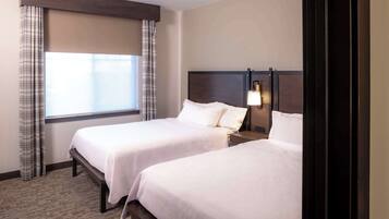 A hotel room with two beds, a window with curtains, a nightstand with a lamp, and a wooden headboard.