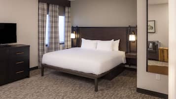 A hotel room with a large bed, a TV on a dresser, a nightstand with a lamp, and a mirror on the wall.