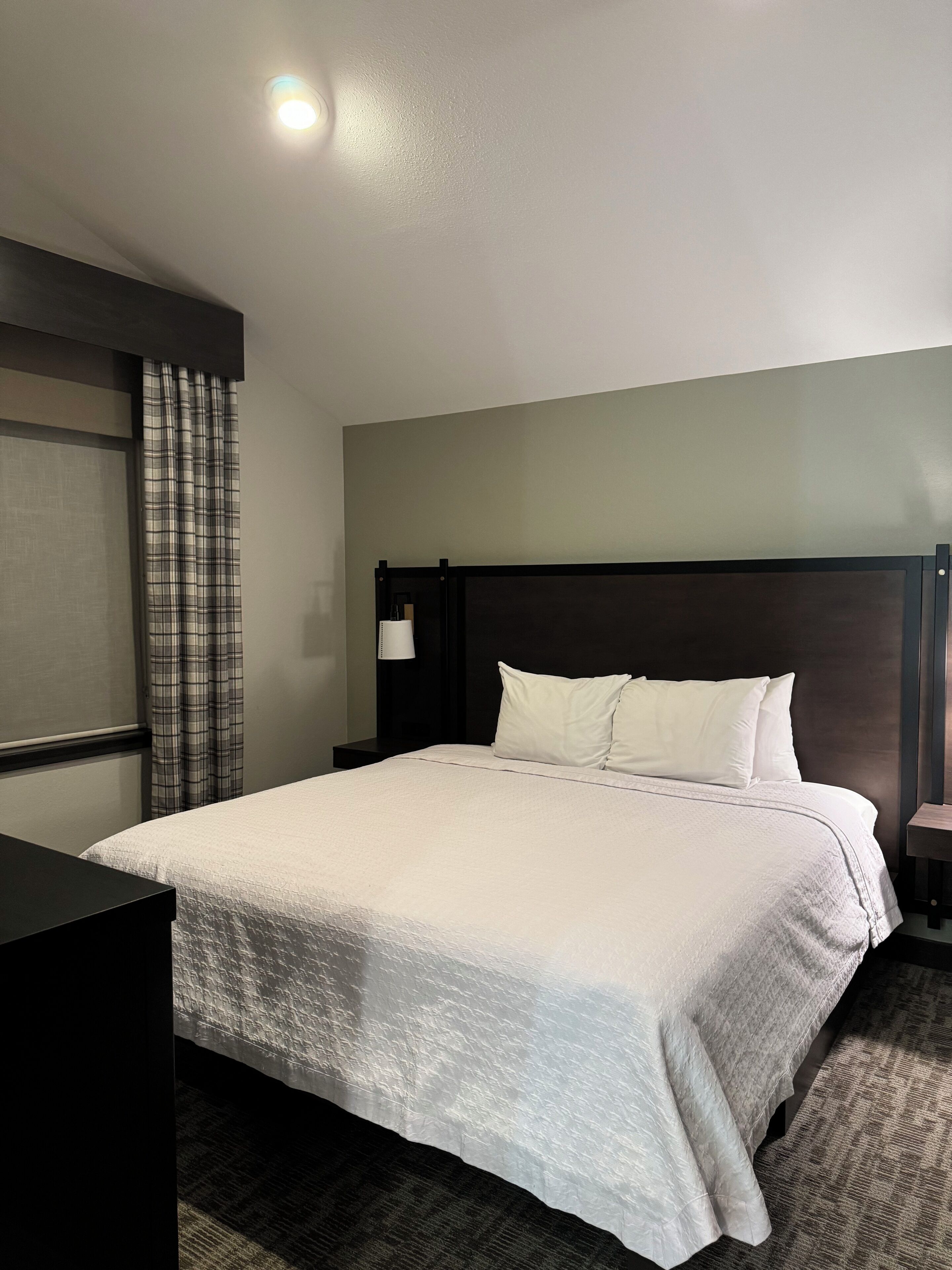 A neatly made bed with white linens, a dark headboard, and a small bedside table with a lamp.