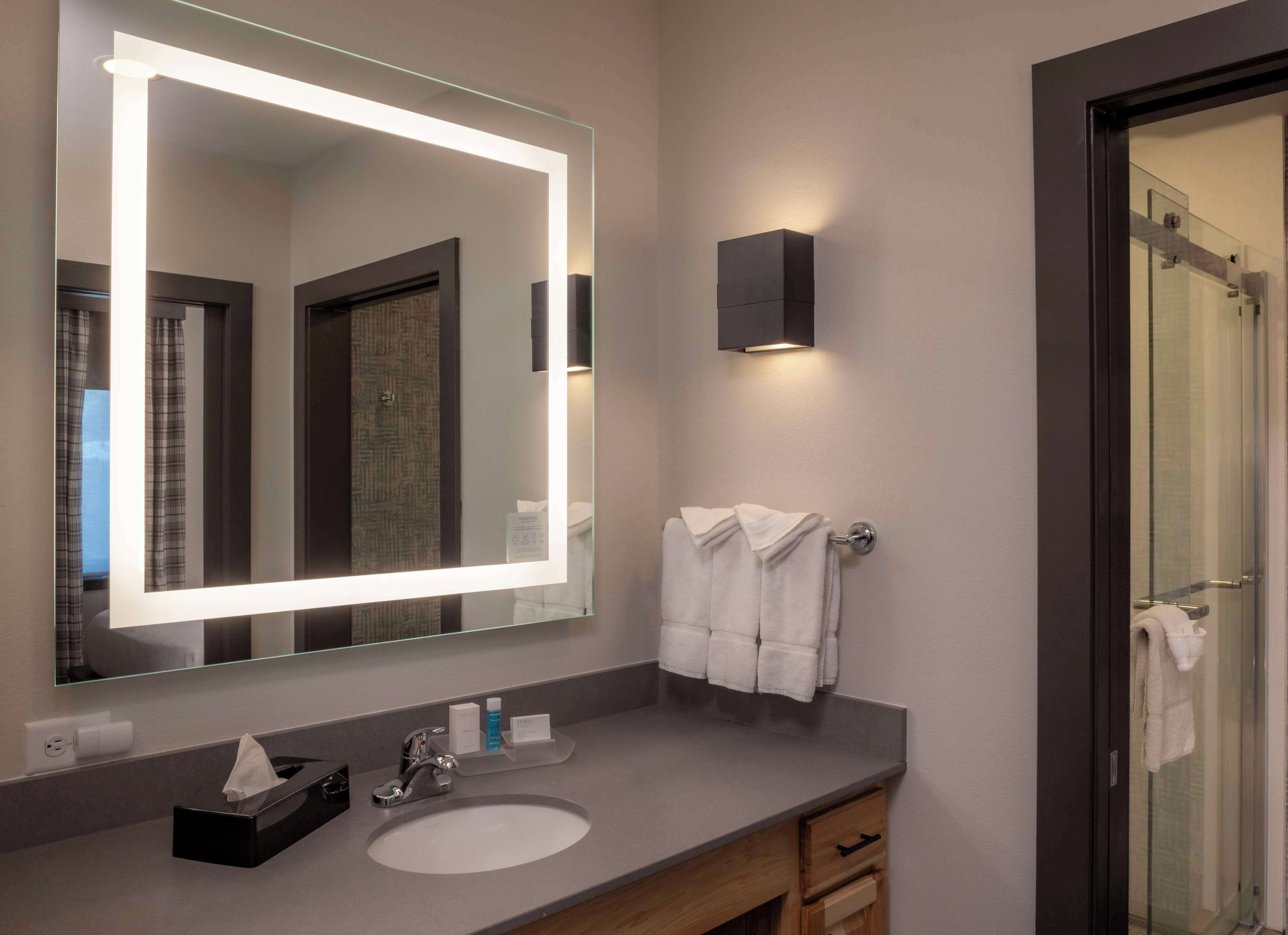 A modern bathroom with a large mirror, a sink, a towel rack, and a glass shower door.