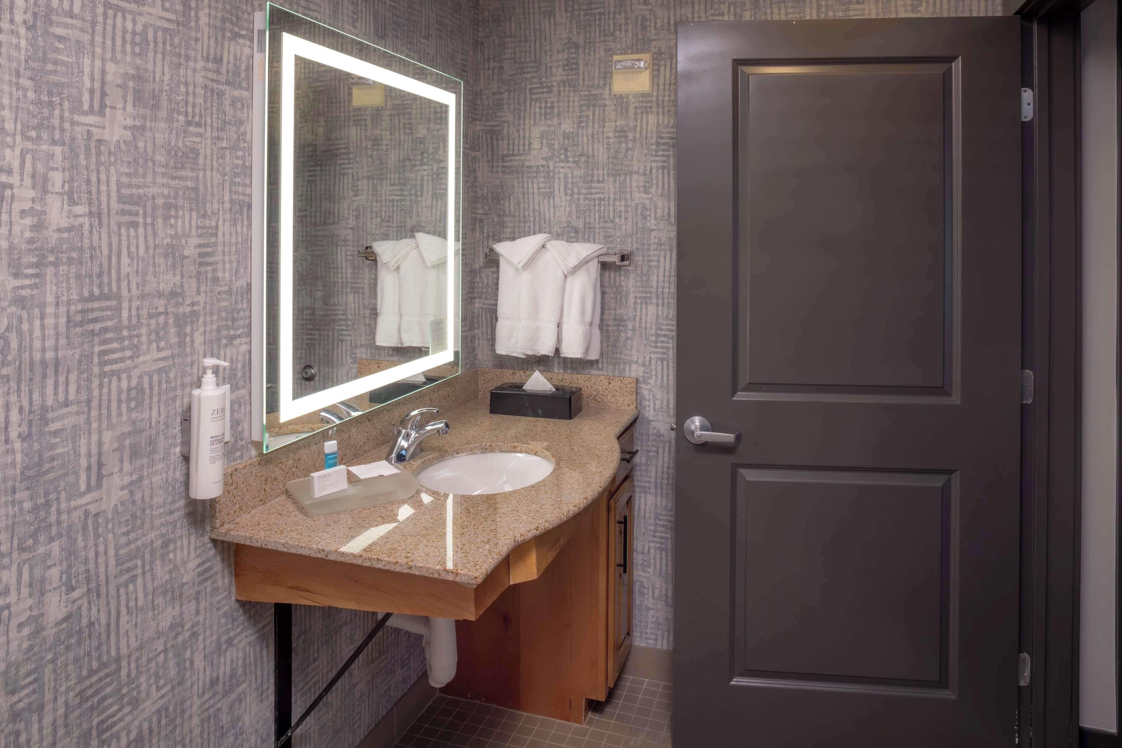 A bathroom with a granite countertop, two sinks, a large mirror, and a towel rack.