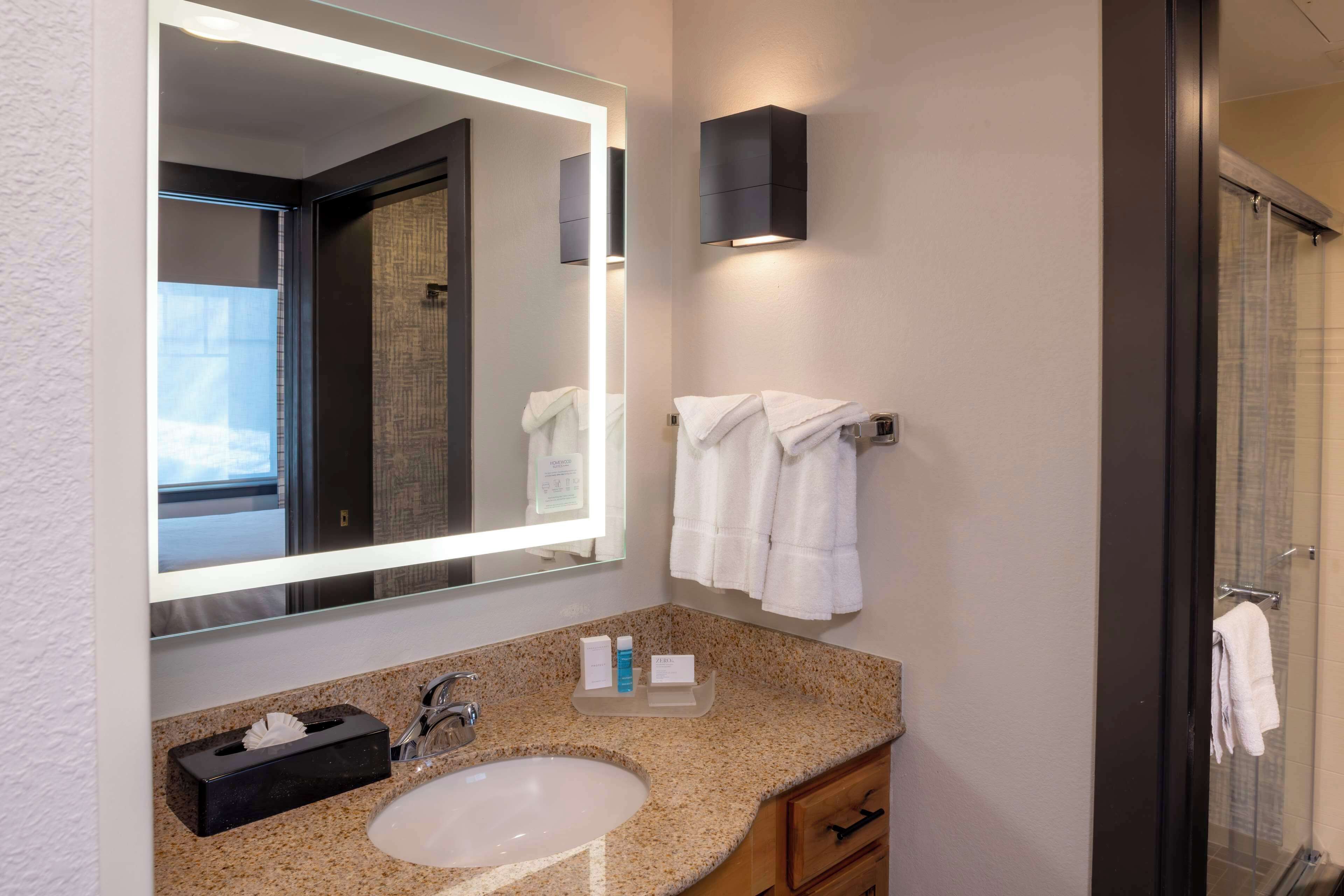 A modern bathroom with a granite countertop sink, a large mirror, and a glass shower enclosure.