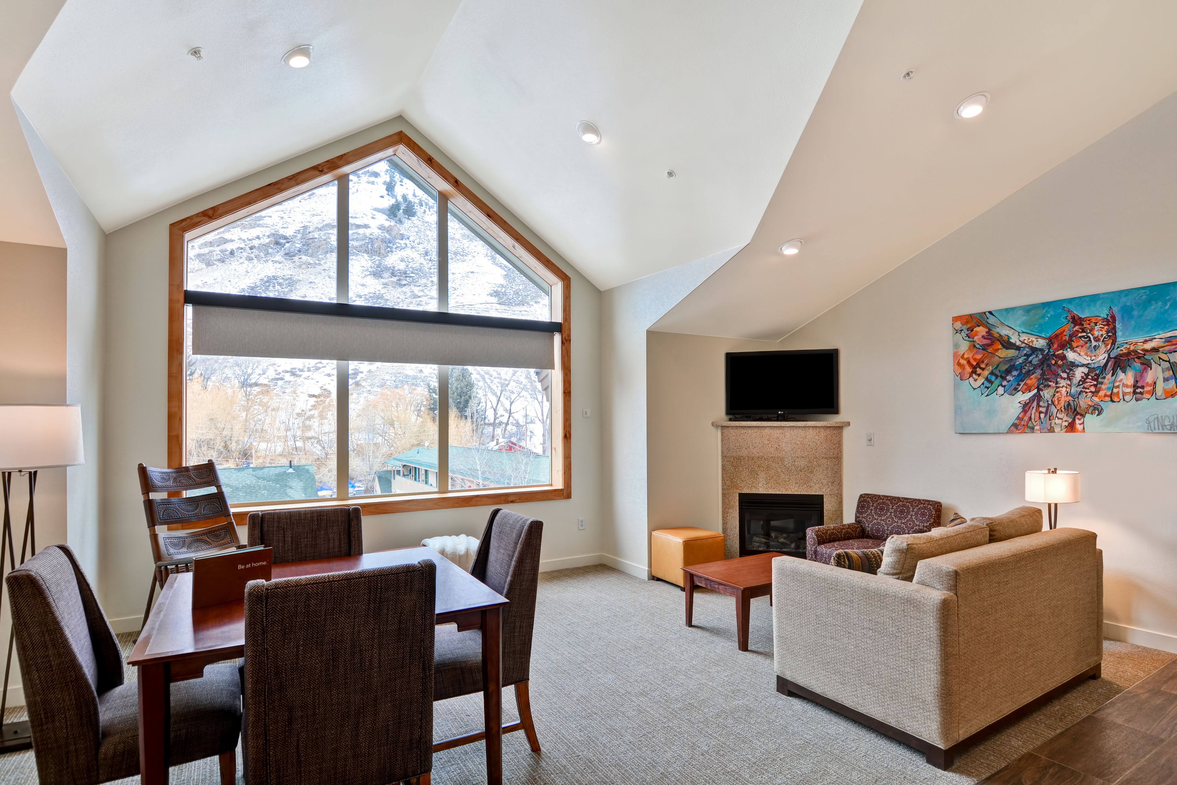 A spacious living room with a large window, a fireplace, and a painting on the wall.