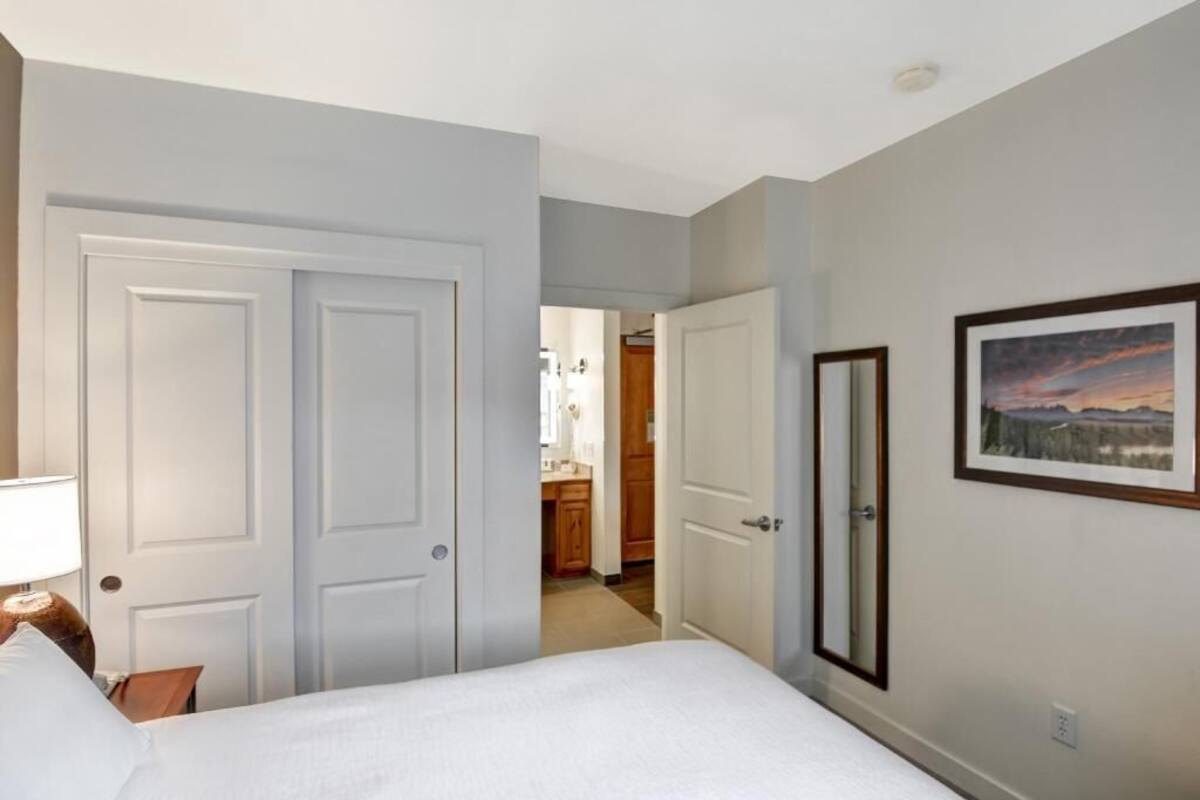 Una camera d'albergo con un letto, una porta, un quadro appeso al muro e un corridoio che conduce a una zona cucina.