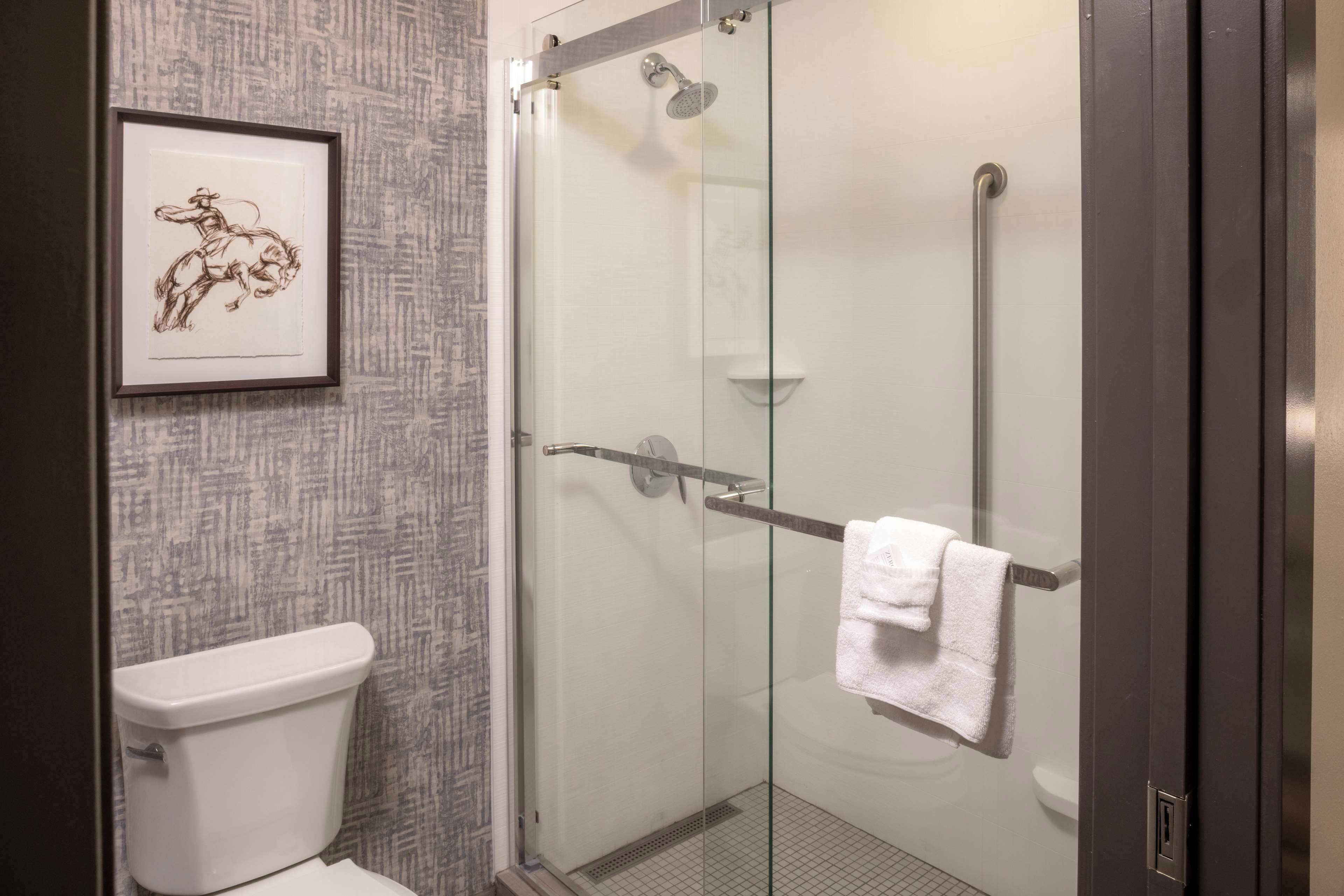 Une salle de bain avec une douche à parois de verre, une œuvre d’art encadrée au mur et une serviette blanche accrochée à la poignée de la porte de la douche.