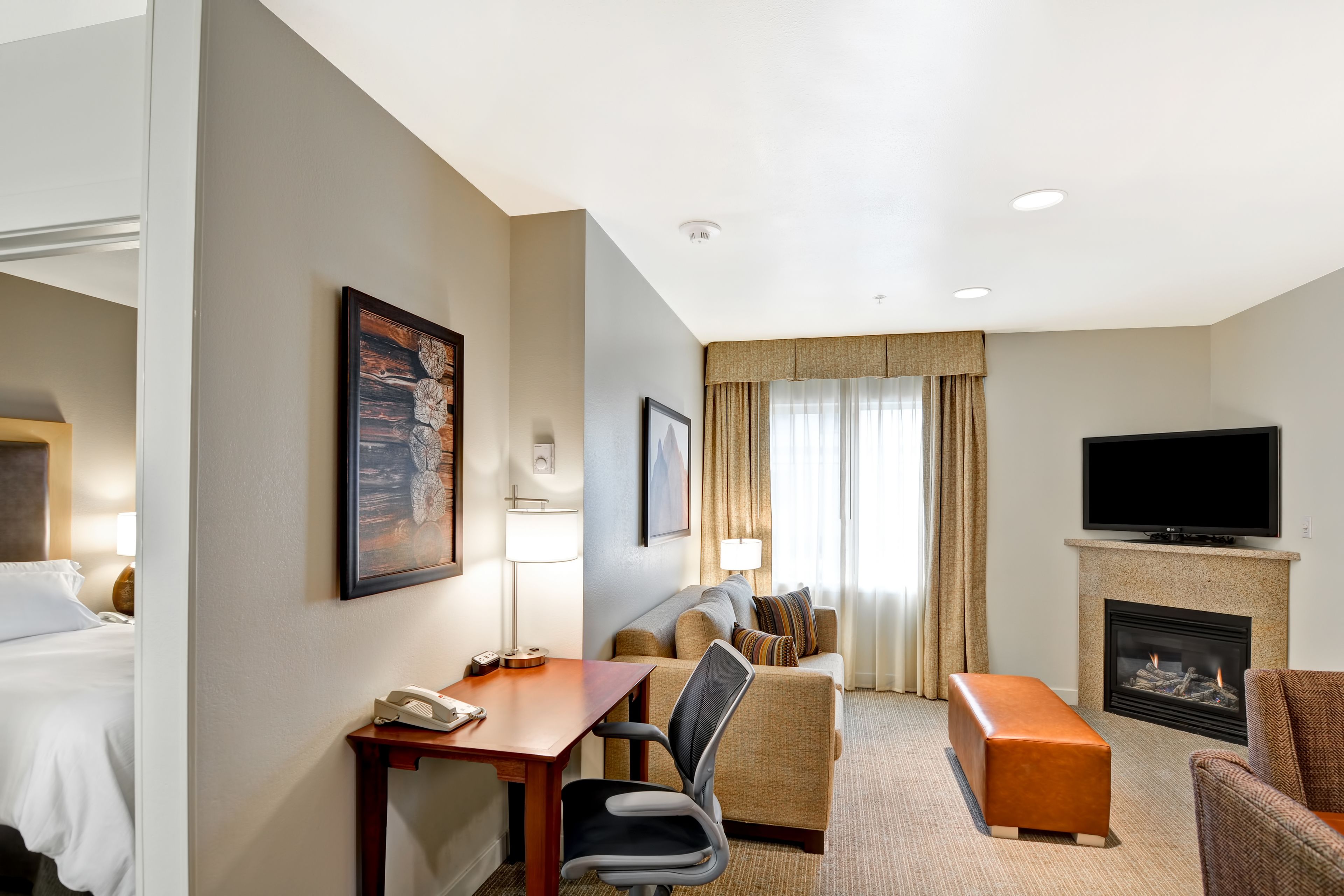 A hotel room with a bed, a desk with a telephone, a chair, a sofa, a television, and a fireplace.