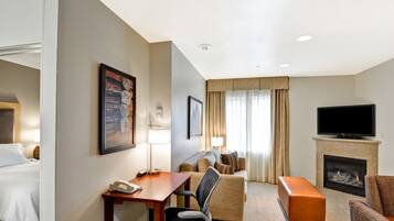 A hotel room with a bed, a desk with a telephone, a chair, a sofa, a television, and a fireplace.