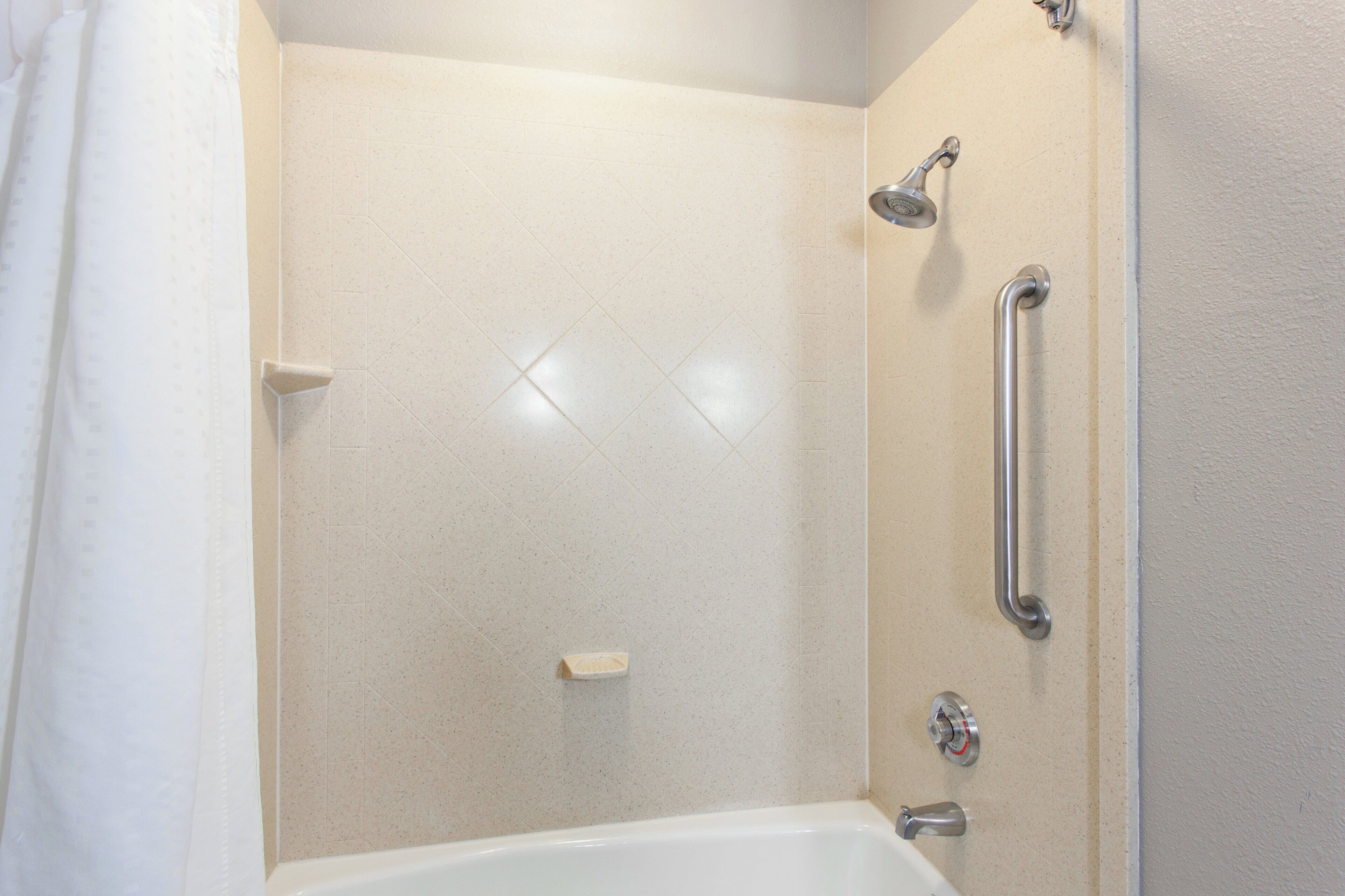 A bathroom with a shower, a grab bar, and a bathtub.