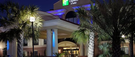 A Holiday Inn Express & Suites hotel with a prominent sign, a covered entrance, and palm trees in the foreground.
