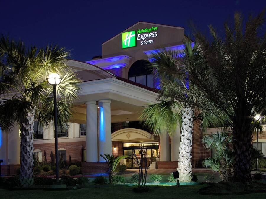 A Holiday Inn Express & Suites hotel with a prominent sign, a covered entrance, and palm trees in the foreground.