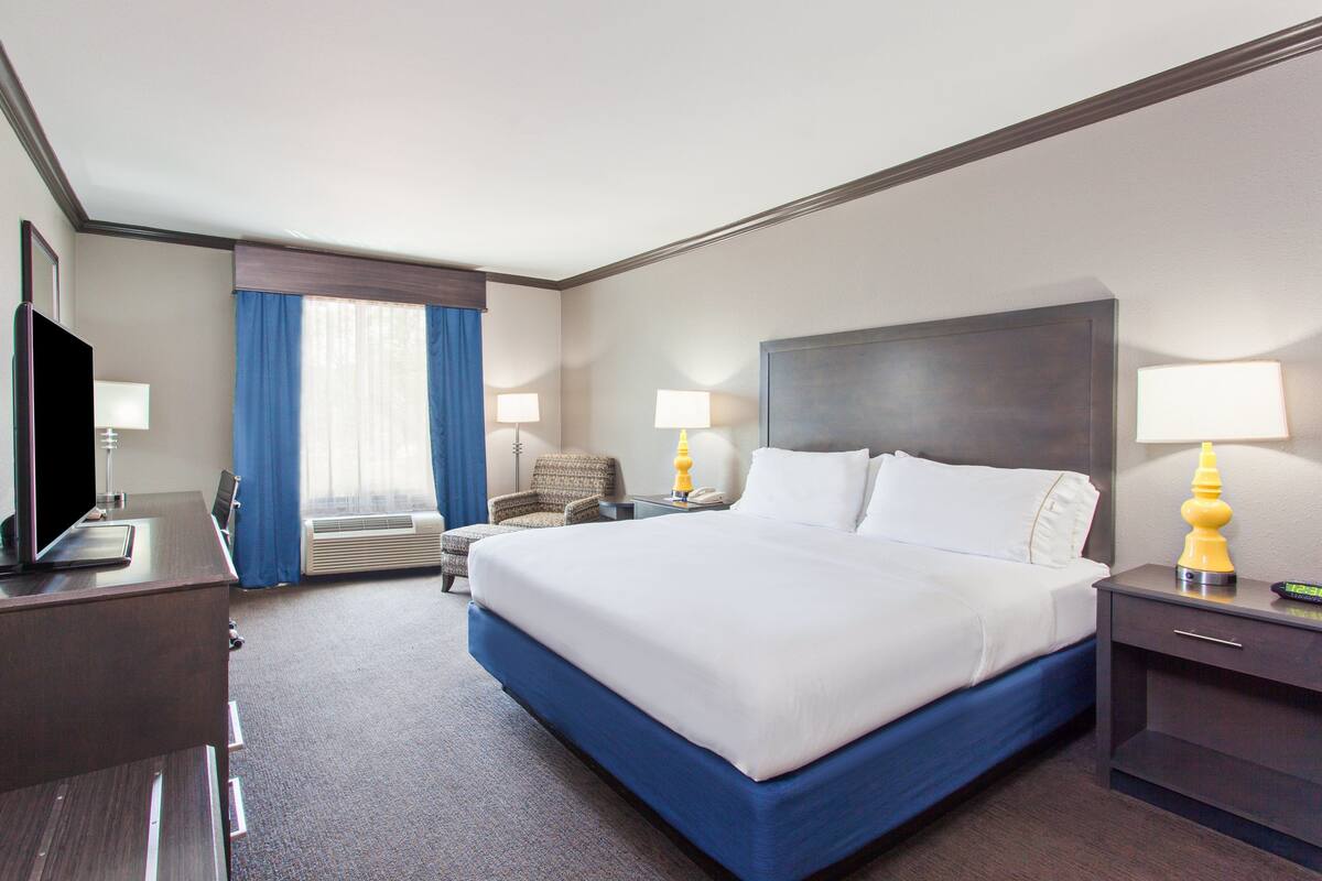 Une chambre d’hôtel avec un grand lit, un bureau avec un ordinateur, une chaise et deux lampes de chevet.