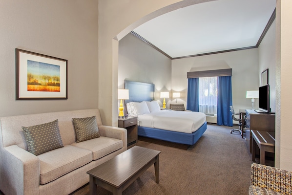 A hotel room with a bed, a sofa, a desk, and a television.