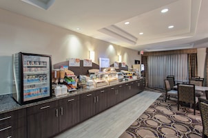 Un área de desayuno de hotel con un mostrador de autoservicio, asientos y vistas de la habitación.