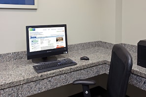 Una computadora de escritorio con un monitor mostrando un sitio web de reservas de hotel, un teclado, un ratón y una silla de oficina negra.