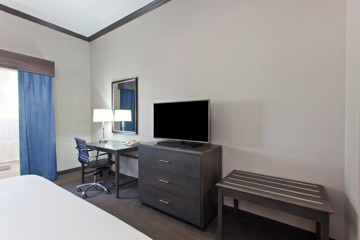A hotel room with a bed, a desk with a computer, a television, a chair, and a small table.