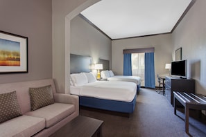 A hotel room with a sofa, two beds, a desk, a TV, and a painting on the wall.