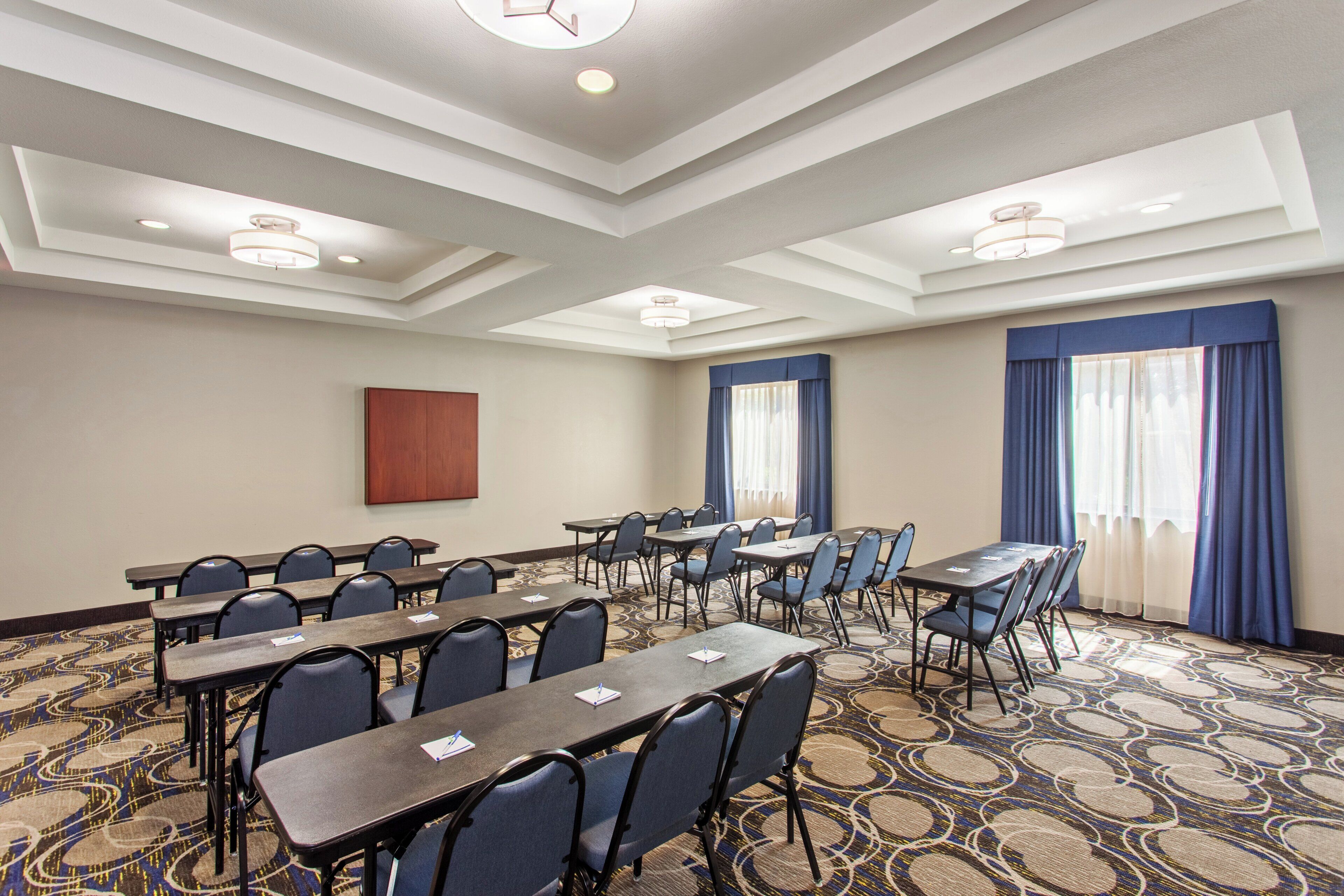 A conference room with multiple tables and chairs, a patterned carpet, and a large window with curtains.