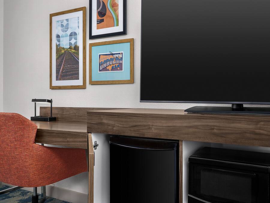 Un salon moderne avec un téléviseur à écran plat, un bureau en bois, une poubelle et un fauteuil rouge.