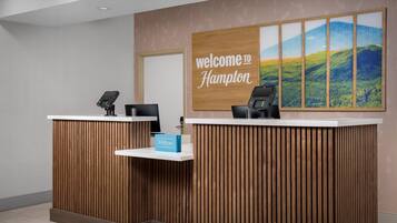 Un comptoir d’accueil avec une pancarte « Bienvenue à Hampton », une carte « Hilton Honors » et une vue panoramique sur les collines.