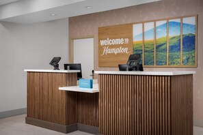 Una mesa de recepción con un cartel que dice 'Welcome to Hampton', una tarjeta de 'Hilton Honors' y una vista panorámica de colinas.