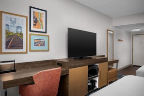 A hotel room with a wooden desk, a flat-screen TV, a red chair, and a bed.