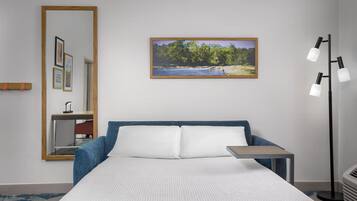 A hotel room with a bed, a bedside table, a mirror, a picture on the wall, and a floor lamp.