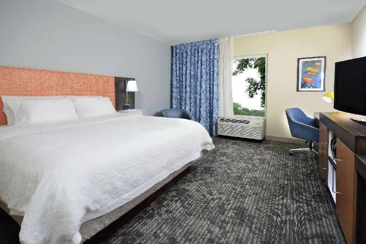 A hotel room with a large bed, a desk with a chair, a television, and a window with curtains.