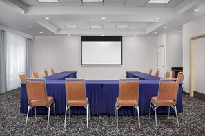 A conference room with a long table, chairs, a projector screen, and a door. - Hampton Inn & Suites Clinton - I-26 (Clinton)