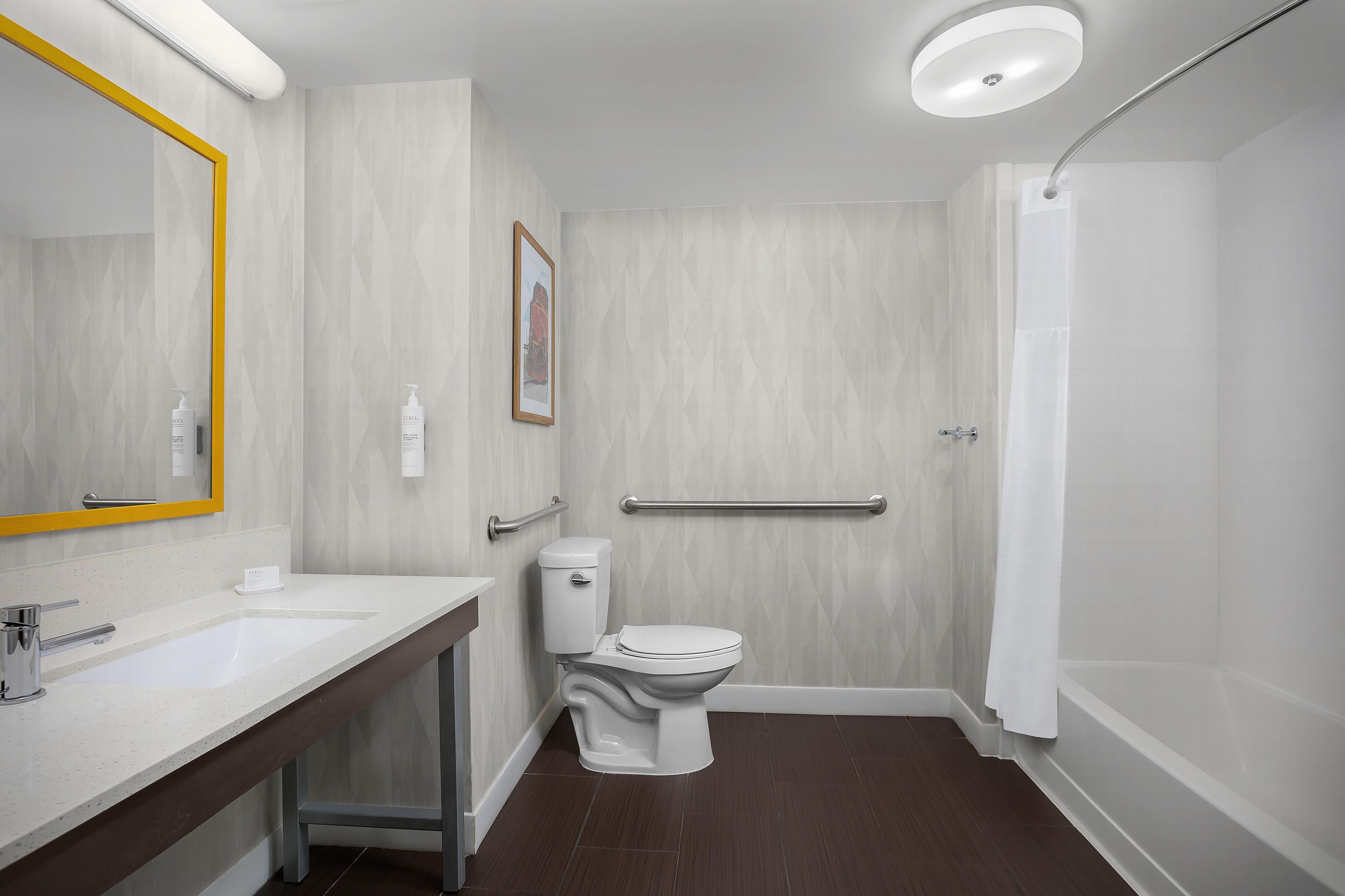 Un baño moderno con inodoro blanco, lavamanos, espejo con marco amarillo y zona de ducha.