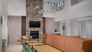A modern interior with a stone fireplace, wooden tables and chairs, and a large orange sofa. - Hampton Inn & Suites Clinton - I-26 (Clinton)