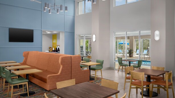 A modern indoor space with a sofa, tables, chairs, and a pool view. - Hampton Inn & Suites Clinton - I-26 (Clinton)