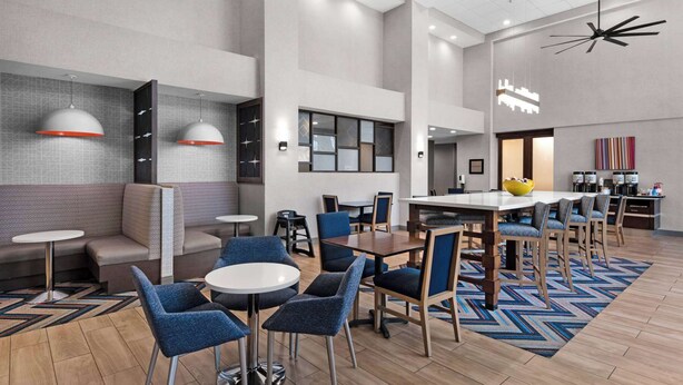 Un moderno vestíbulo de hotel con zonas de estar, una mesa de comedor central y un ventilador de techo.