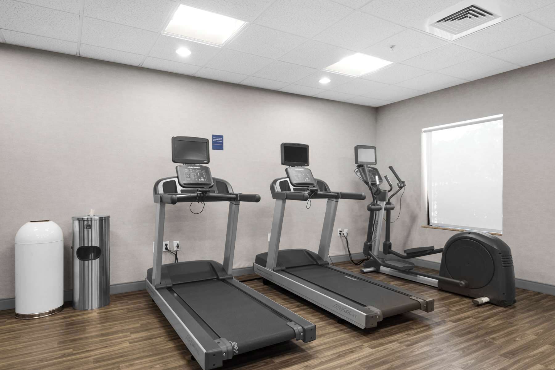 Ein Fitnessraum mit drei Laufbändern, einem Ergometer und zwei Mülleimern.