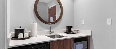 A modern bathroom with a sink, mirror, coffee maker, and a microwave.
