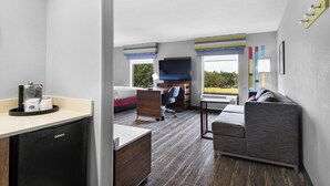Una habitación de hotel compacta con kitchenette, una cama, un sofá, un escritorio y un televisor.
