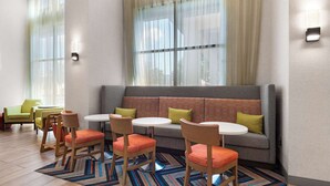 Una habitación de hotel moderna con un sofá, sillas y mesas dispuestas alrededor de un gran ventanal con cortinas traslúcidas.