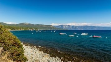 A coastal scene with boats on calm waters, rocky shoreline, and distant mountains.