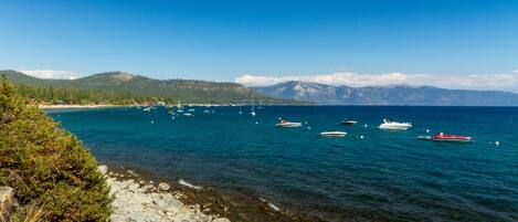 A coastal scene with boats on calm waters, rocky shoreline, and distant mountains.