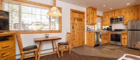Una cocina moderna con armarios de madera, electrodomésticos de acero inoxidable, un comedor con mesa y sillas, y un amplio ventanal que proporciona luz natural.