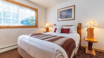 A hotel room with a large bed, two bedside lamps, a window with blinds, and a framed picture on the wall.