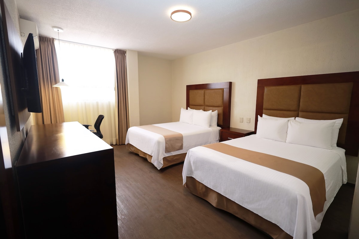Habitación de hotel con dos camas, un escritorio y un televisor.