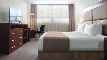 A hotel room with a bed, a desk, a chair, a TV, and curtains.