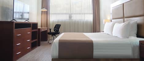 Una habitación de hotel con cama, escritorio, silla, televisor y cortinas.